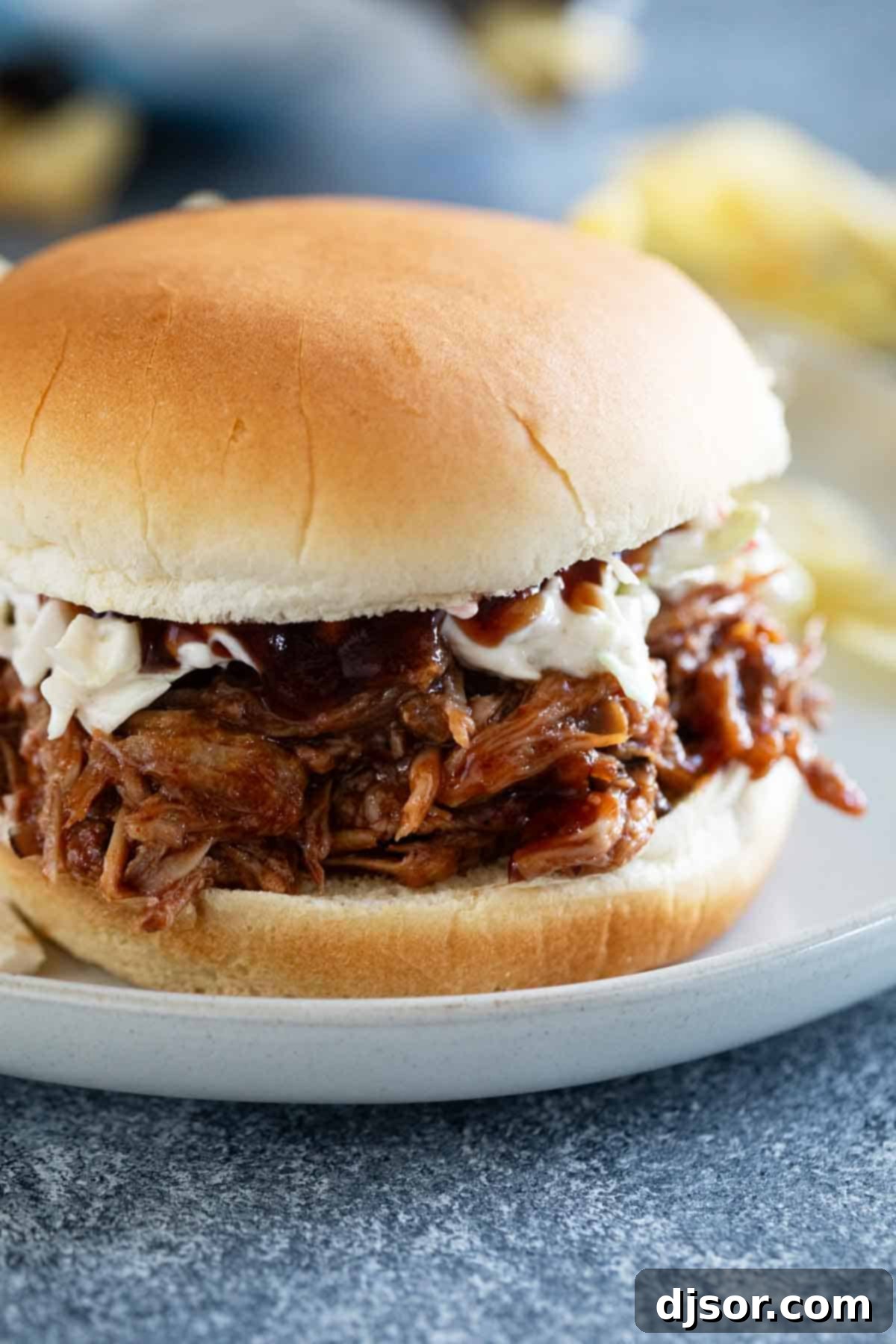 A delicious Slow Cooker Pulled Pork sandwich topped with creamy coleslaw, served on a light bun.
