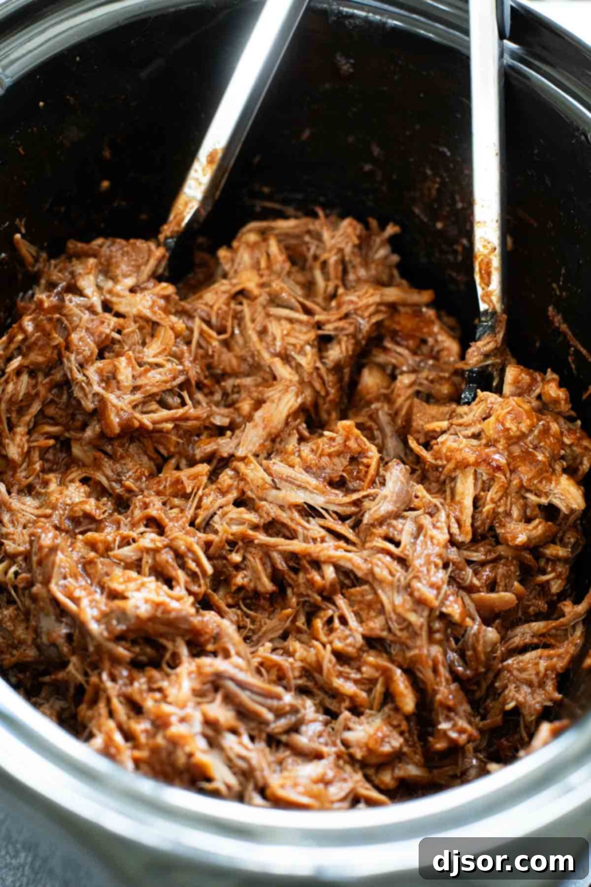 A close-up shot of a slow cooker filled to the brim with perfectly cooked, saucy BBQ pulled pork, ready to be served.