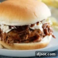 A delicious Slow Cooker Pulled Pork sandwich topped with creamy coleslaw, served on a light bun.
