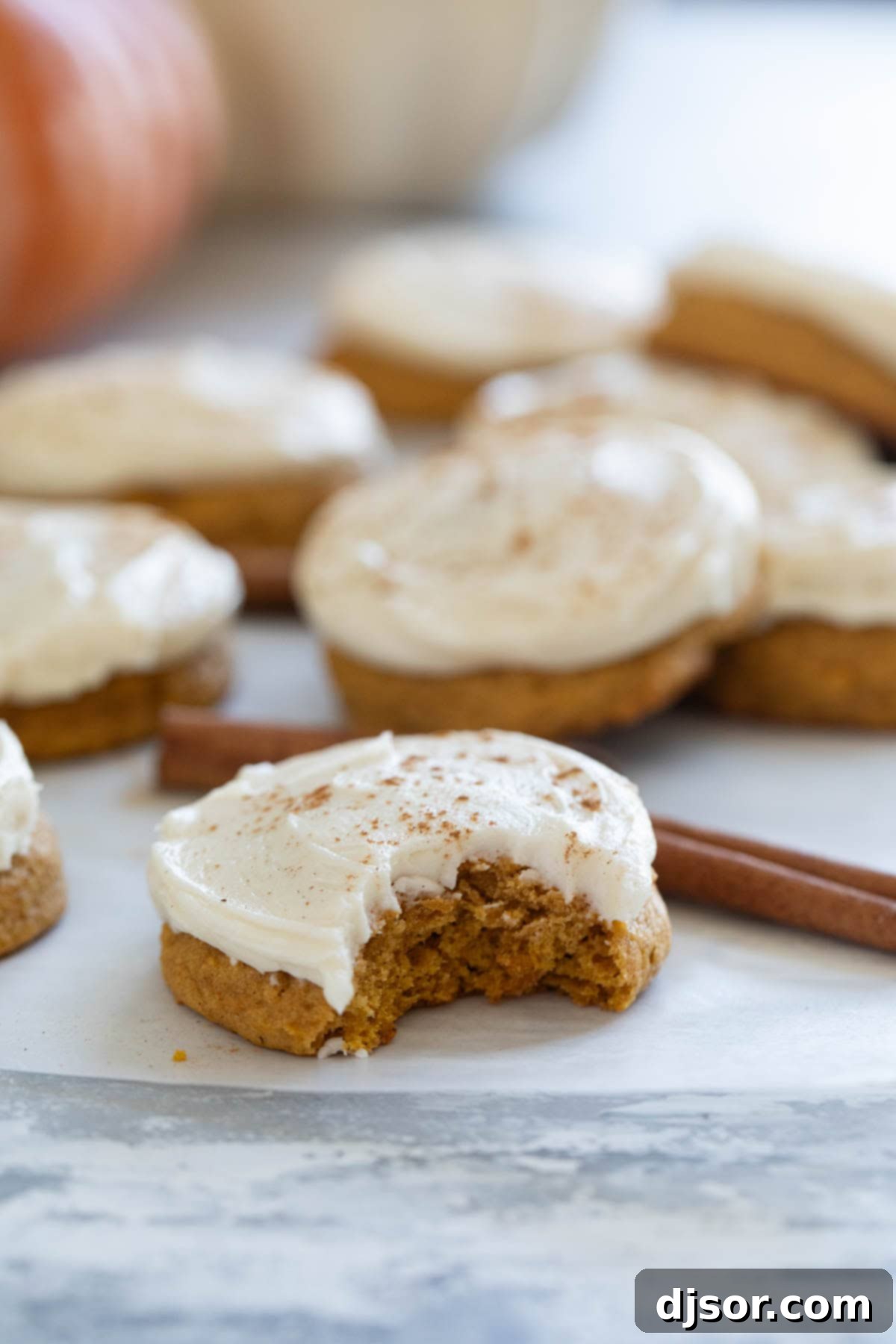 Cream Cheese Frosted Pumpkin Spice Cookies 8 Pumpkin Cookies with Cream Cheese Frosting with a bite taken from one cookie.