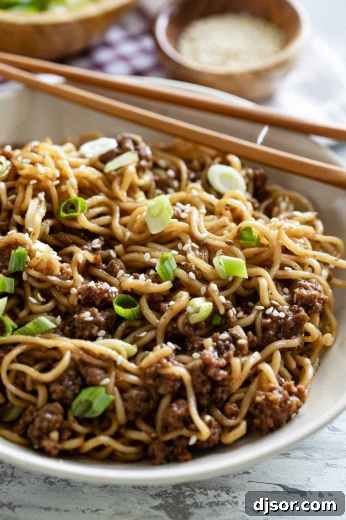 A vibrant bowl of Mongolian Ground Beef Noodles, generously garnished with fresh green onions and toasted sesame seeds, ready to be enjoyed.