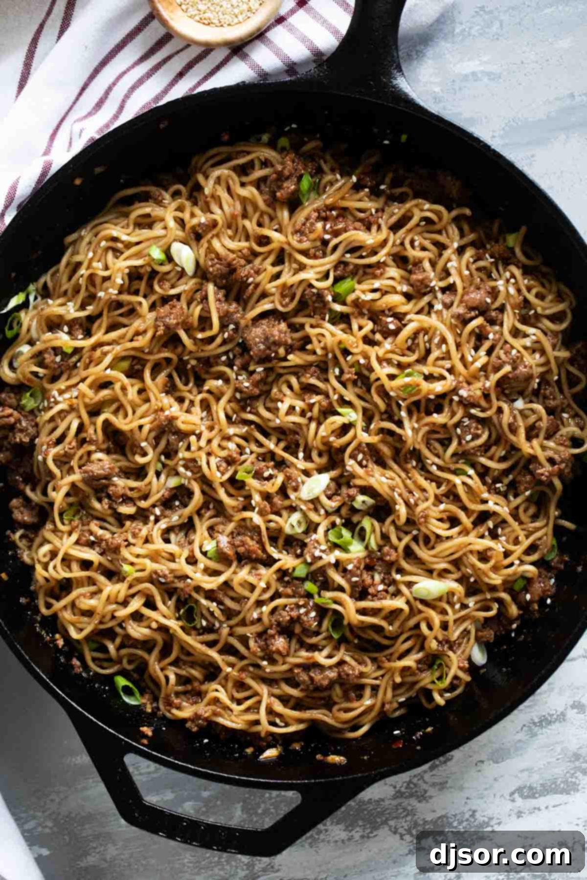 A cast iron skillet overflowing with steaming Mongolian Ground Beef Noodles, showcasing the rich sauce and perfectly coated noodles.