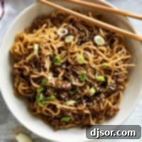A beautifully presented bowl of Mongolian Ground Beef Noodles, garnished with green onions and sesame seeds, with a pair of chopsticks resting on the side, inviting you to dig in.