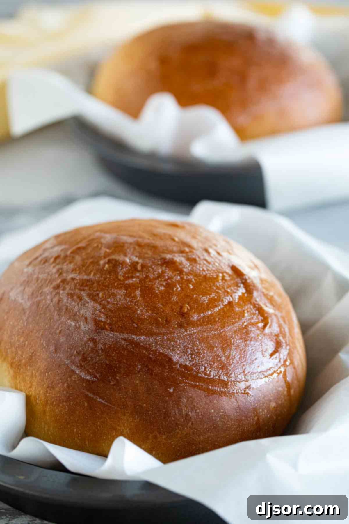 Soft and slightly sweet, this Hawaiian Bread is the perfect side dish to any Hawaiian meal. Serve it up as a side with butter, and save a loaf for French toast the next day! Three perfectly baked round boules of Hawaiian Bread, nestled in parchment paper in cake pans, ready to be enjoyed.