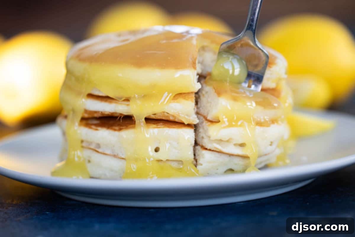 Fluffy pancakes topped with luscious lemon sauce, a delightful breakfast treat. A close-up of a stack of pancakes drenched in golden lemon sauce, adorned with a fresh lemon slice and mint sprig.