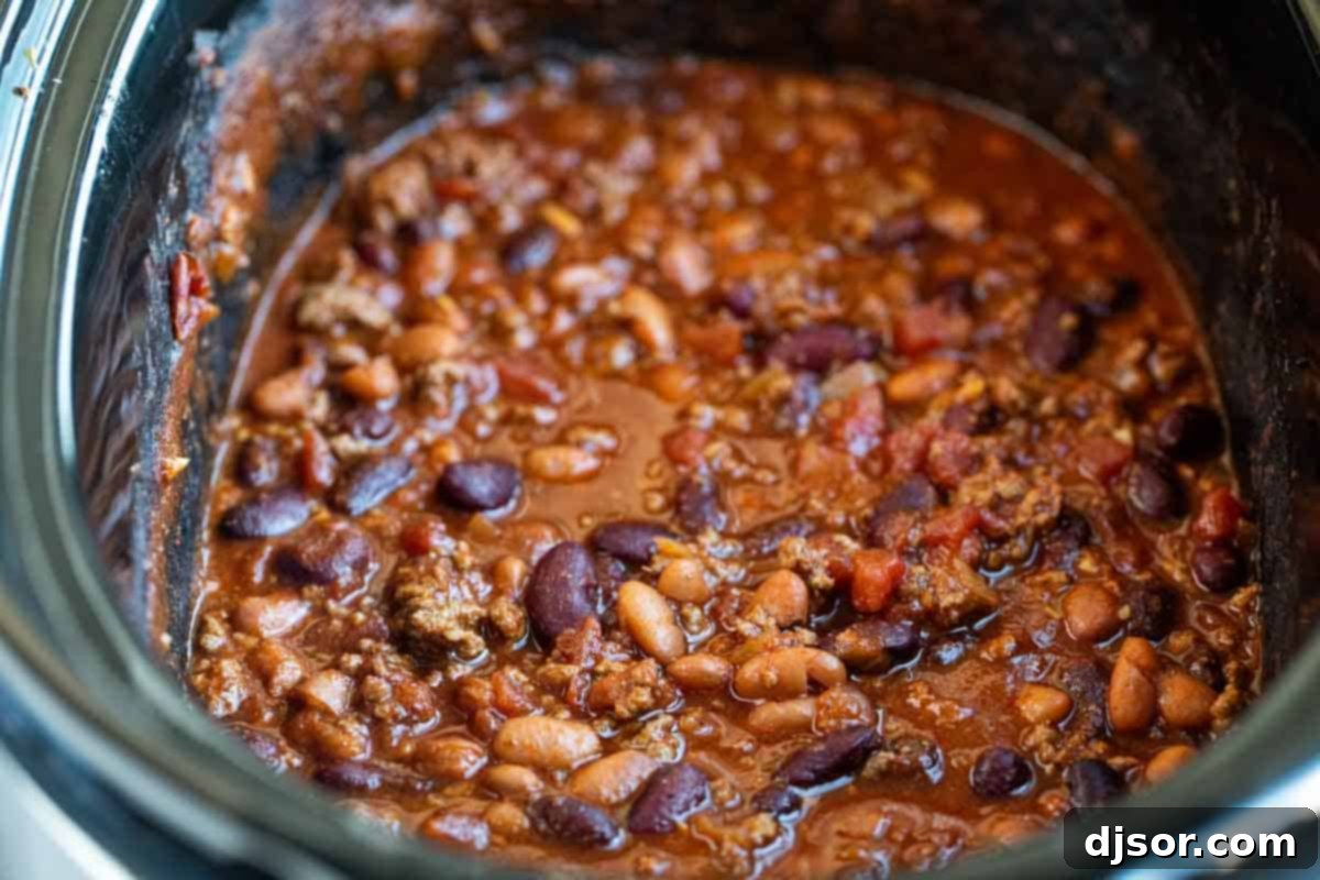 Close-up view of rich, simmering crock pot chili in a slow cooker, showing the hearty texture of ground beef, beans, and tomatoes, ready to be served.
