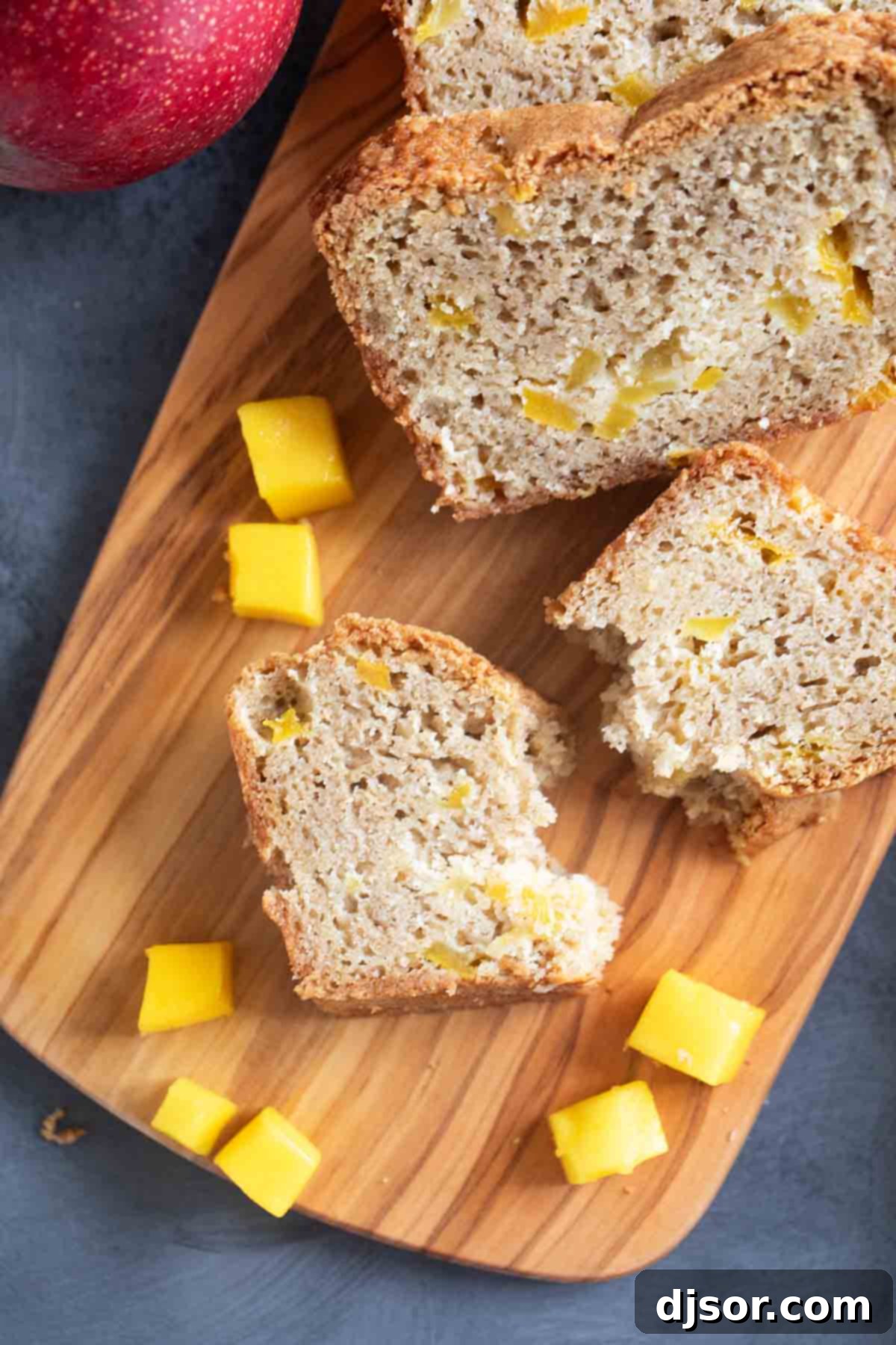 Beautifully sliced mango bread with one slice gently broken in half to reveal the moist interior and mango chunks.