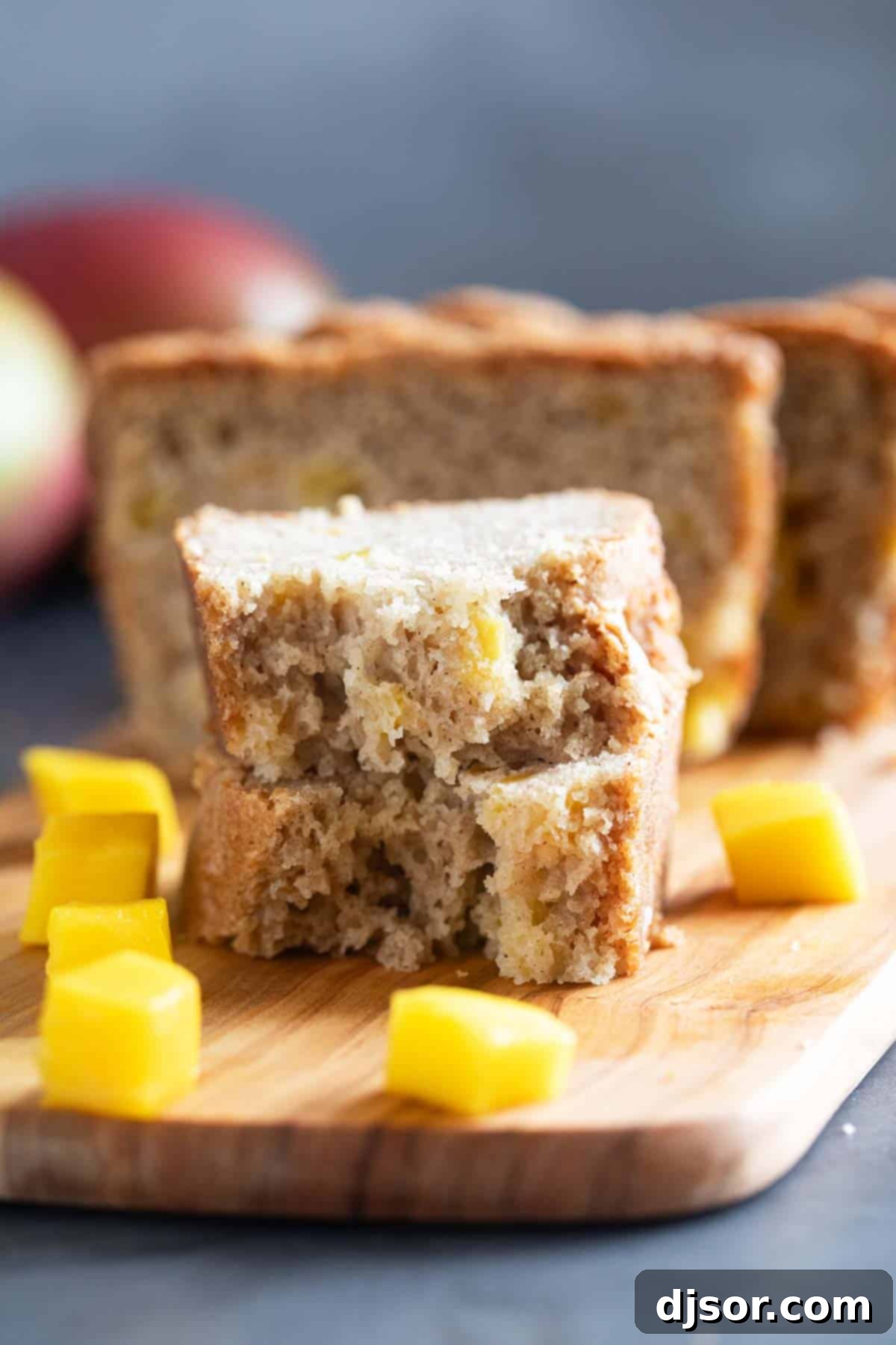 A broken half slice of mango bread artfully stacked with other slices, highlighting the fluffy texture and fruit pieces.