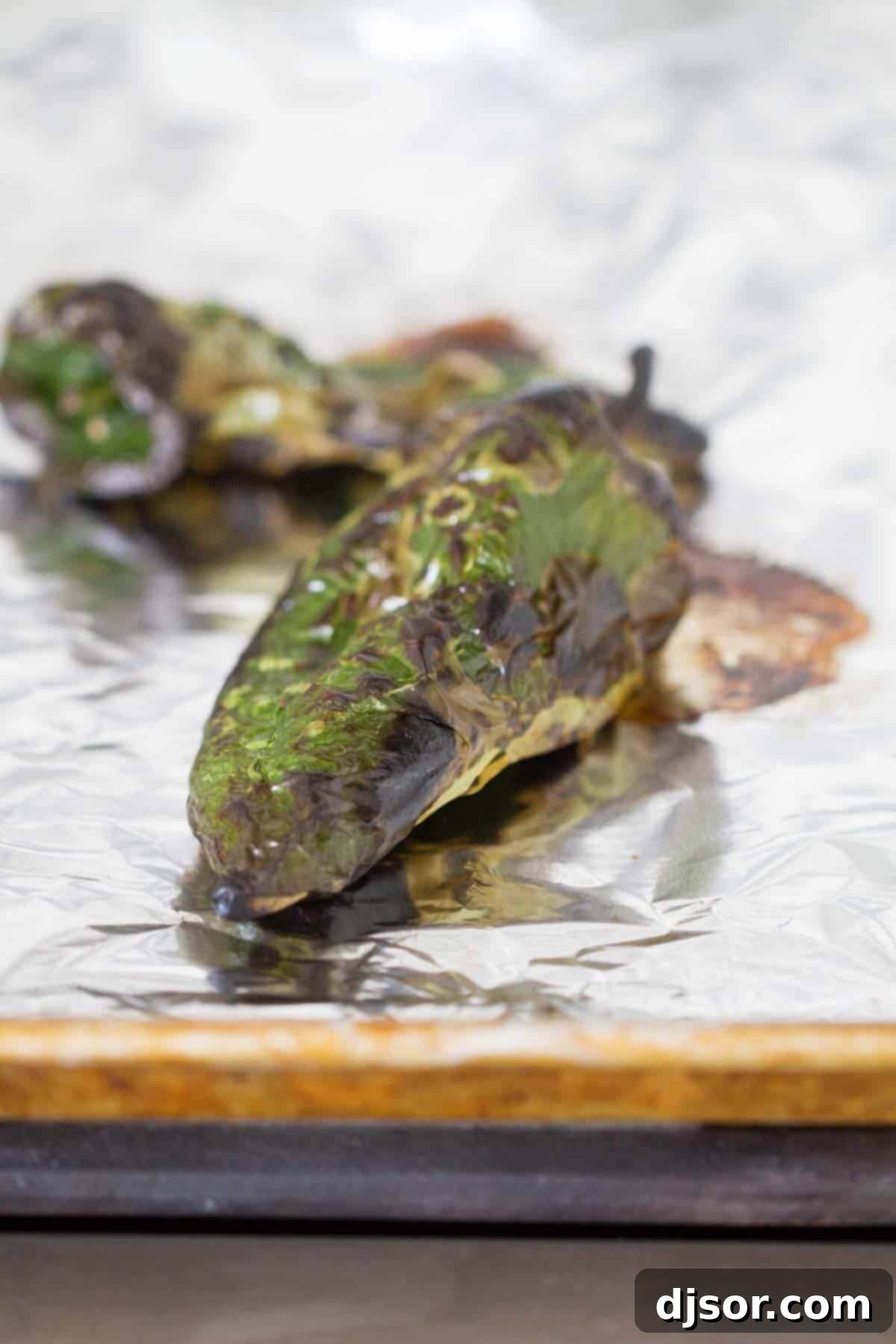Close-up of charred poblano peppers on a foil-lined baking sheet.