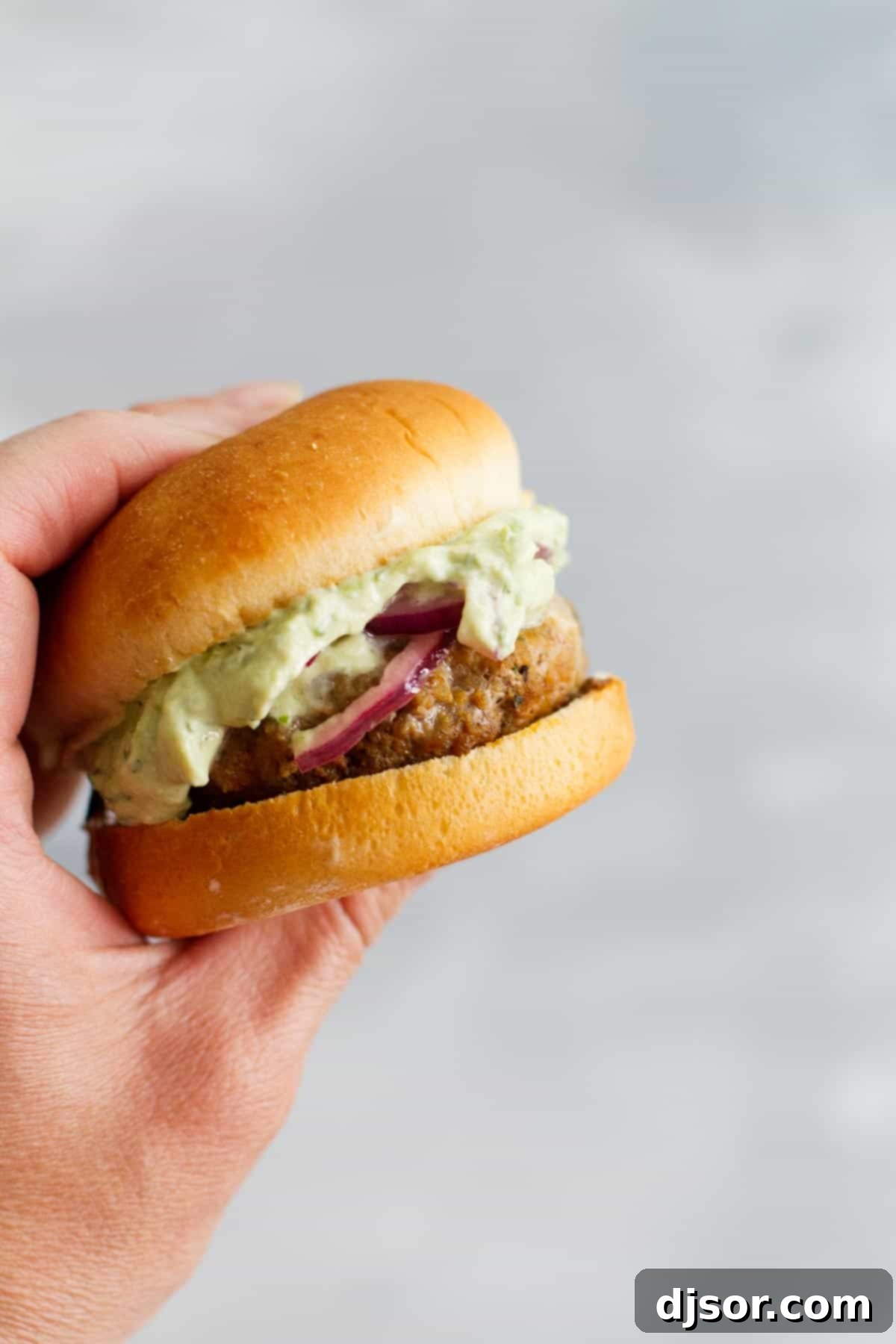A hand holding a perfectly assembled poblano pepper slider burger, showcasing its layers.