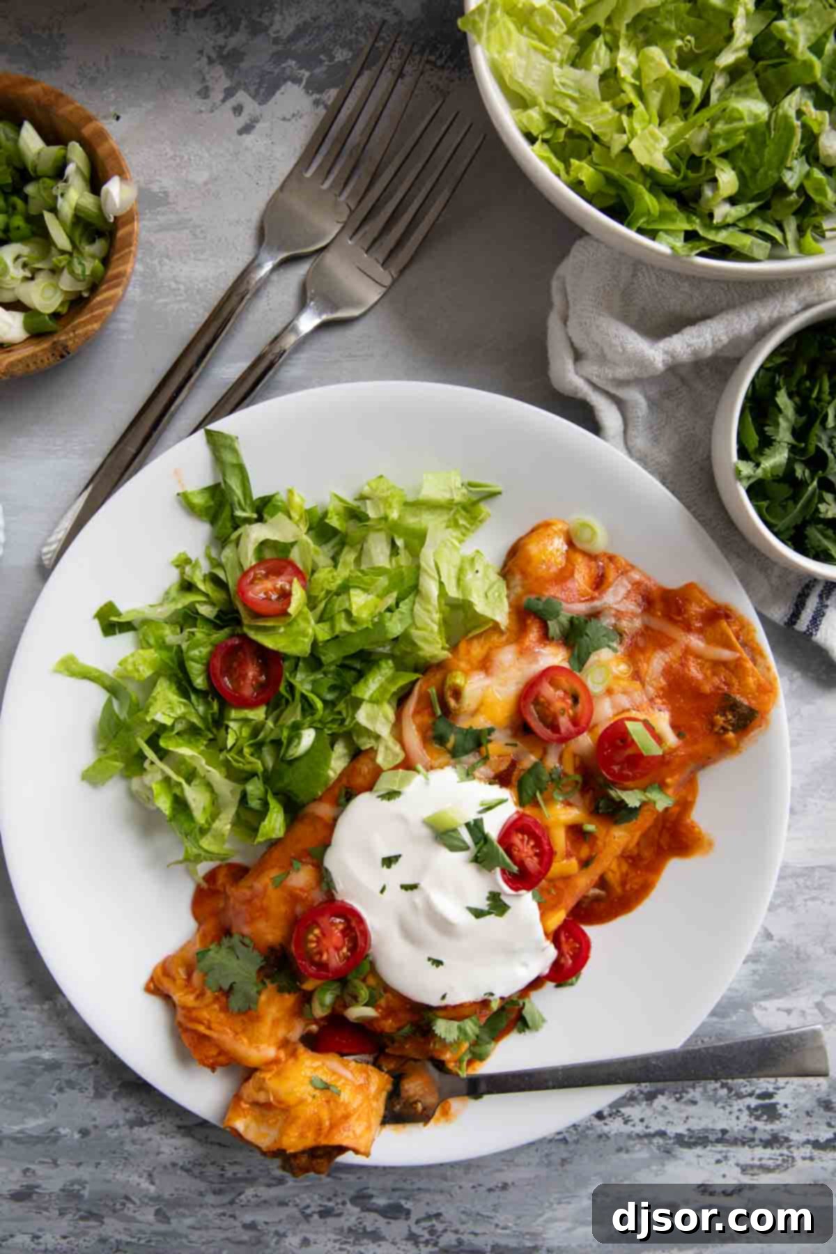 Cheesy Beef Enchilada Bake 10 Ground beef enchiladas garnished with sour cream, diced tomatoes, and fresh cilantro, served in a casserole dish.