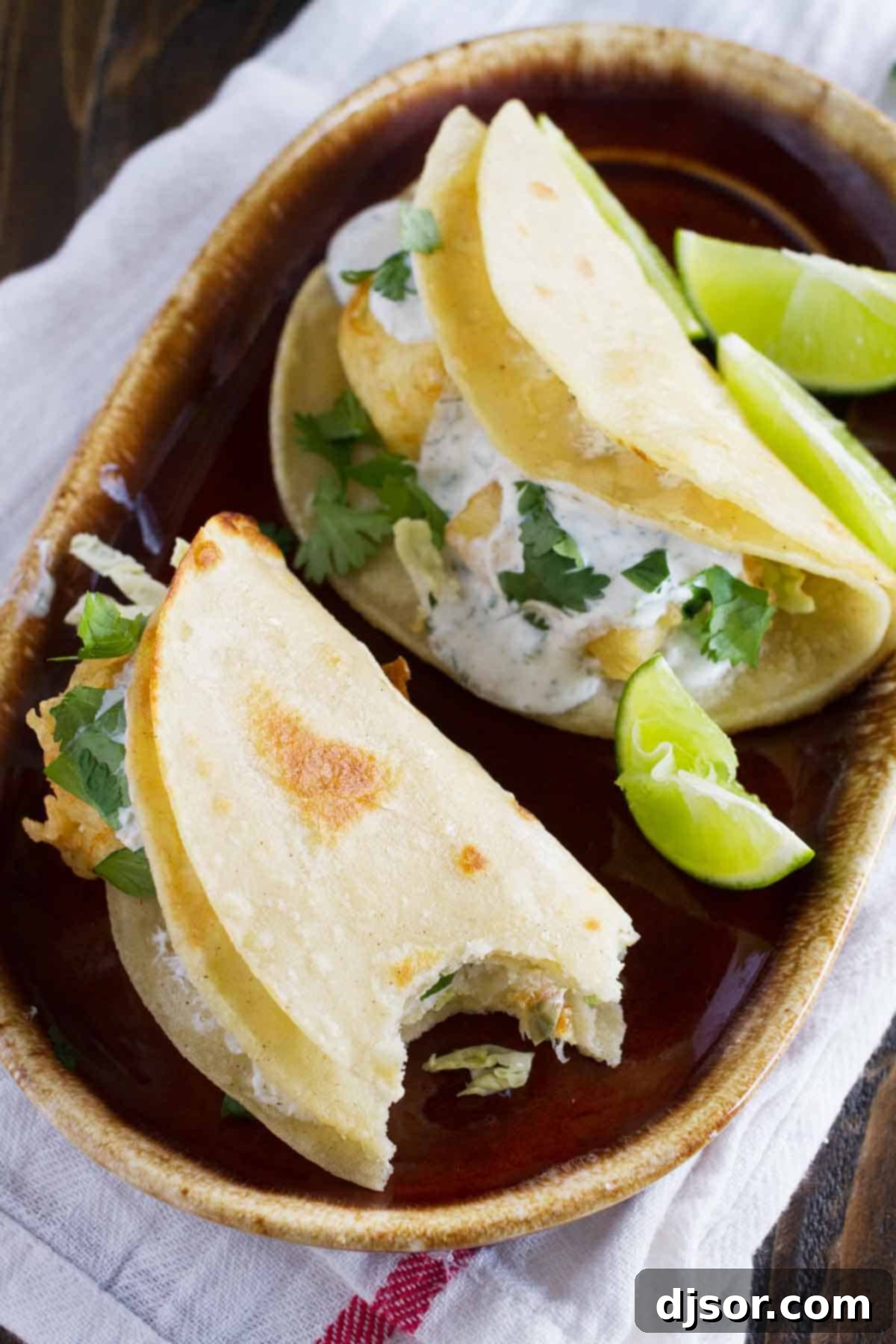 A taste of San Diego, these fried fish tacos have pieces of battered, fried fish inside corn tortillas, topped with a creamy, tangy white sauce. Close-up of fried fish tacos with generous white sauce and fresh toppings