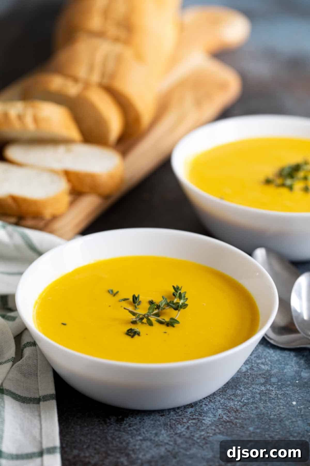 Two bowls of creamy butternut squash soup garnished with fresh herbs, with crusty bread in the background, signaling a warm and inviting meal.