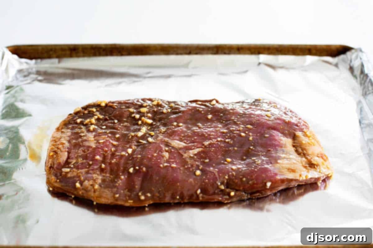 Marinated flank steak ready for cooking on a foil-lined baking sheet.