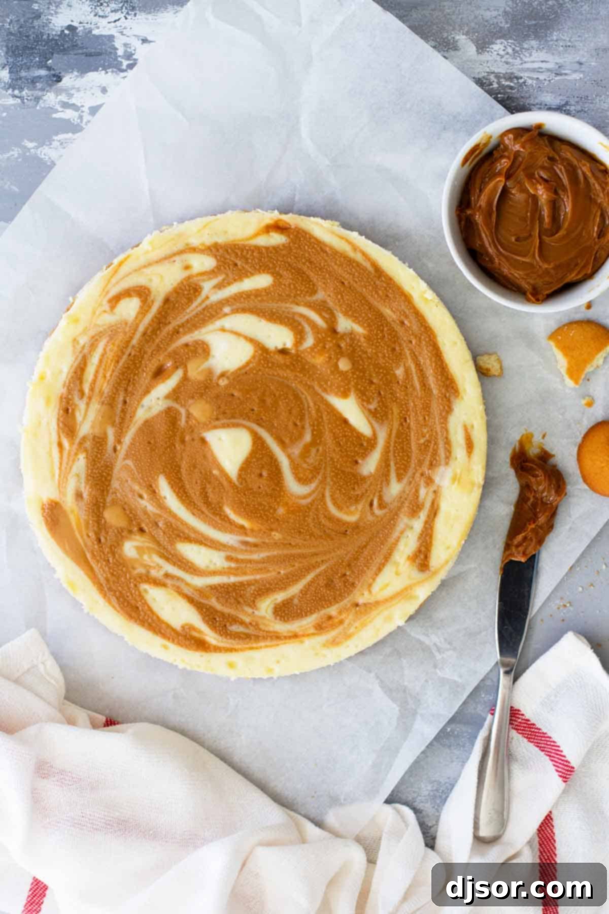 A creamy cheesecake is swirled with dulce de leche in this decadent and delicious Dulce de Leche Cheesecake. This creamy cheesecake is holiday worthy! A whole Dulce de Leche Cheesecake presented with a side of extra dulce de leche for drizzling, highlighting its rich caramel swirl.
