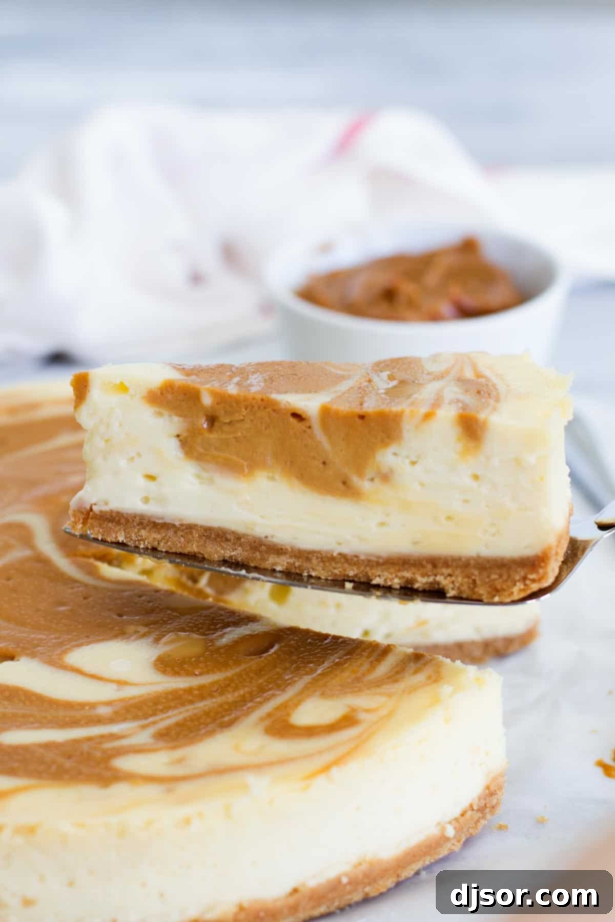 A slice of creamy Dulce de Leche Cheesecake being served from the full dessert, highlighting its perfect texture and rich caramel swirls.