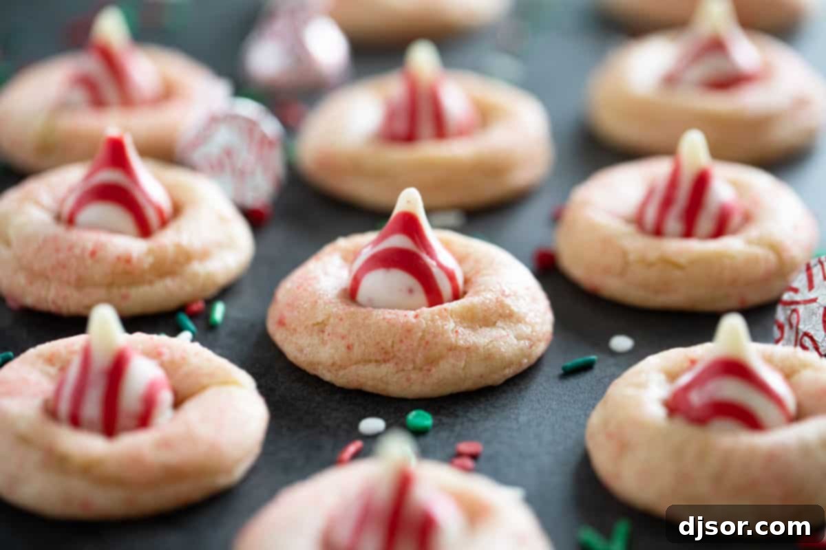 Peppermint Kiss Cookies surrounded by sprinkles and kisses, showcasing their soft texture and pink shimmer.