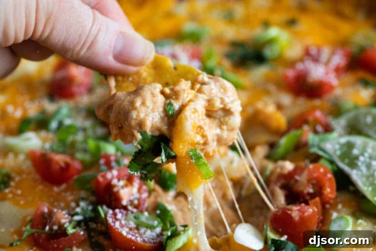 Enjoying Cheesy Bean Dip with Tortilla Chips A tortilla chip being dipped into a warm, cheesy bean dip in a skillet, showing the gooey texture.