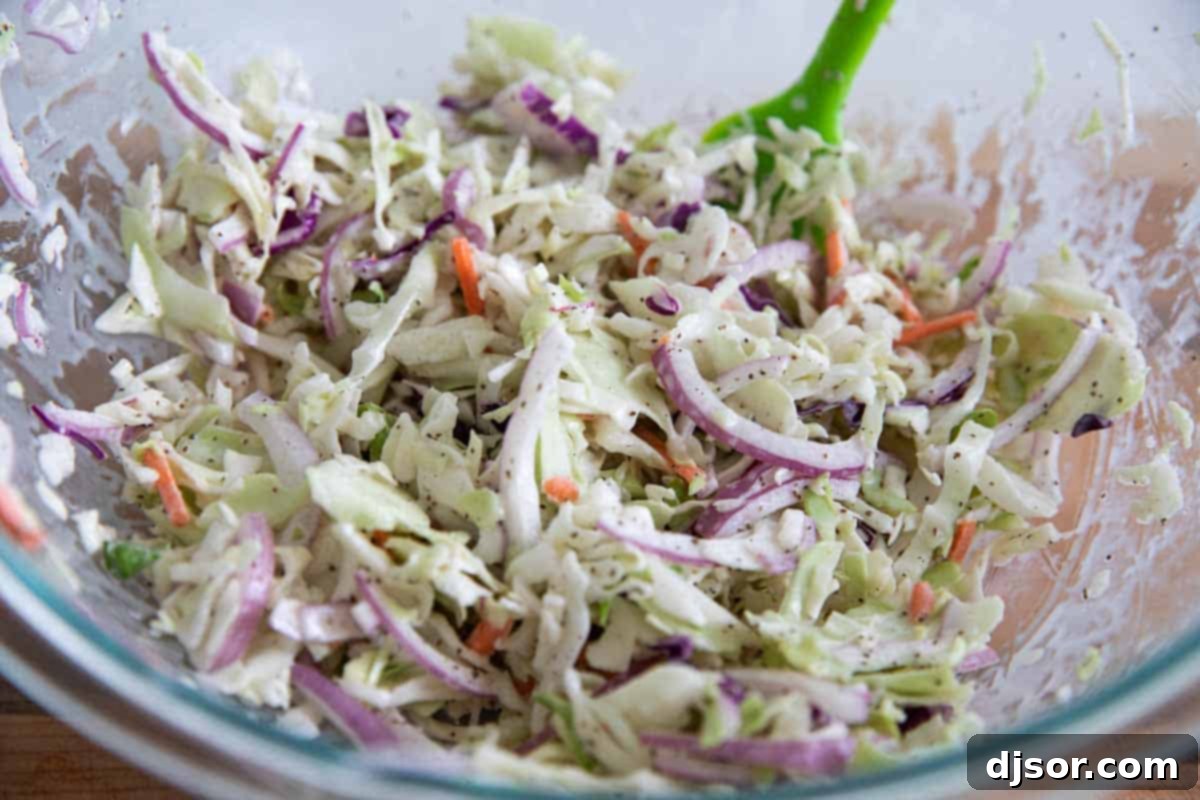 A bowl of fresh, vibrant coleslaw ready to be served, featuring shredded cabbage, carrots, and thinly sliced red onion in a creamy dressing.