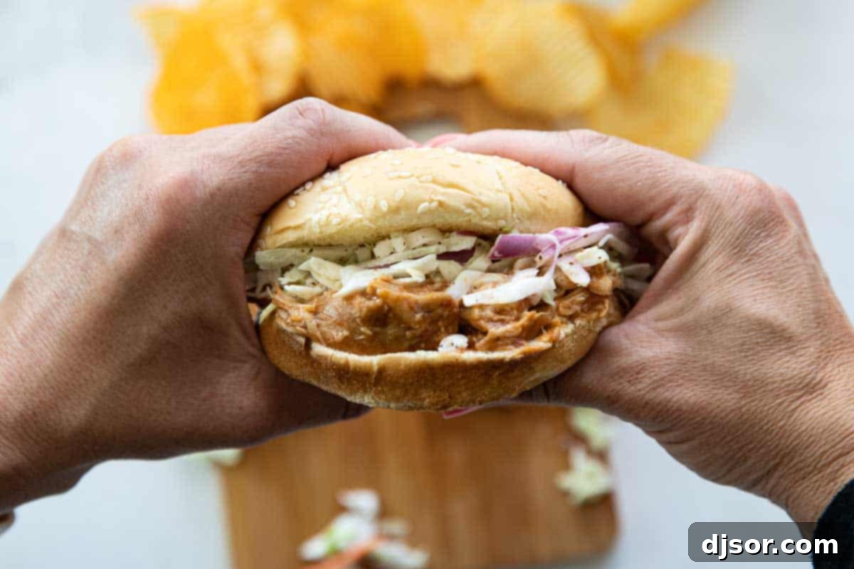 A hand holding a delicious Slow Cooker Teriyaki Chicken Sandwich with coleslaw, ready to be enjoyed.