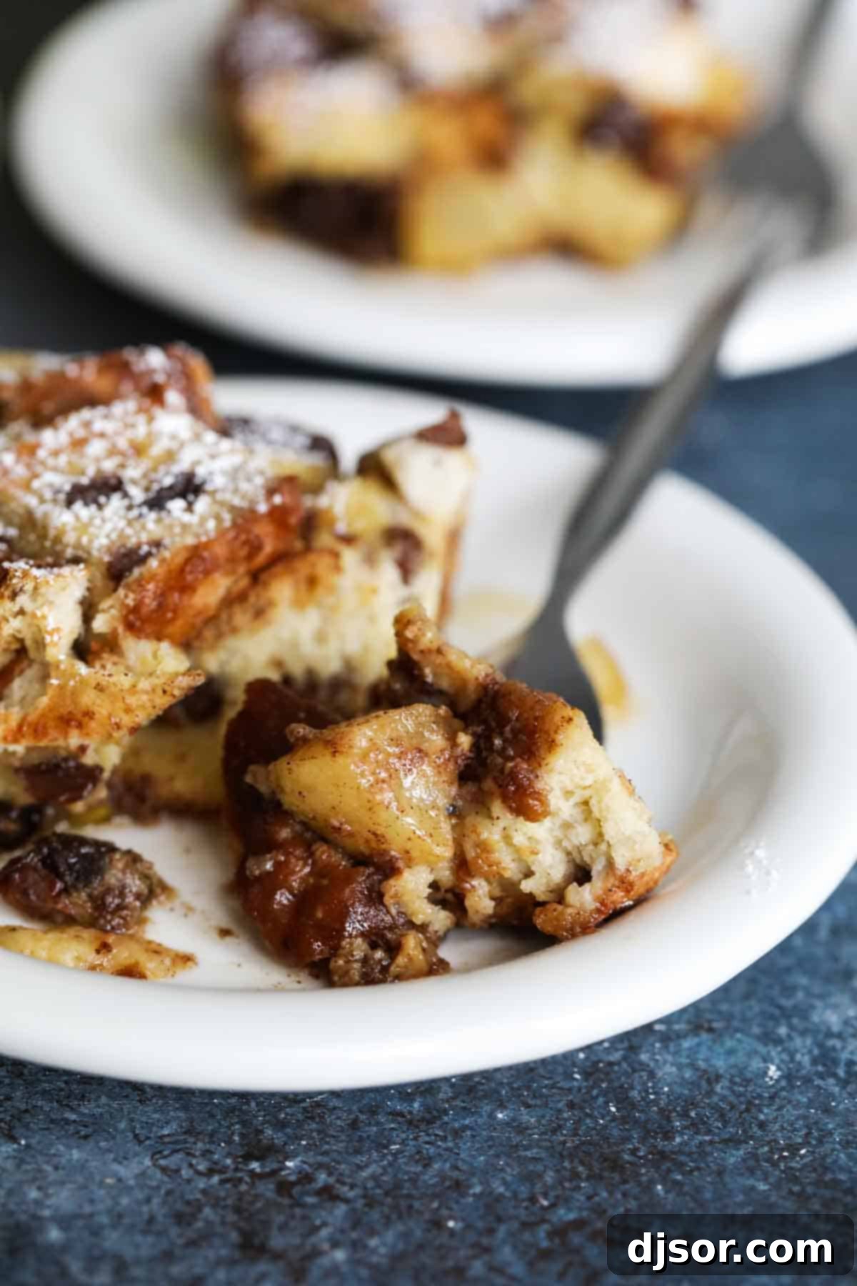 Slice of baked French toast casserole with apples and raisins with a bite taken from it.