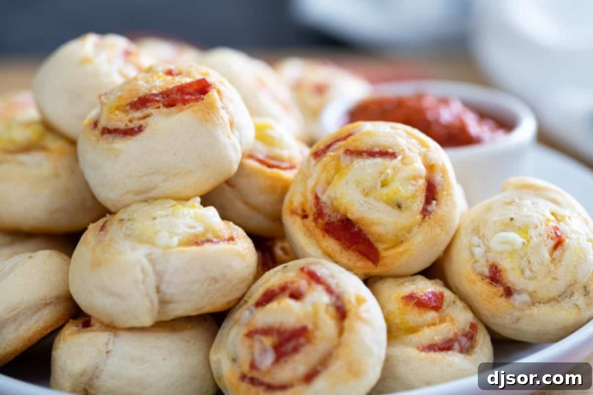 Cheesy Pepperoni Swirls 2 Pepperoni Pinwheels stacked on a plate with dipping sauce, showcasing their golden crust and savory filling.