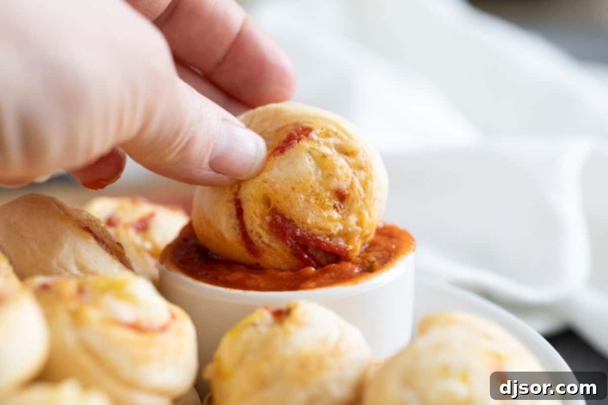 Cheesy Pepperoni Swirls 8 Close-up shot of a hand dipping a pepperoni pinwheel into a small bowl of marinara sauce.