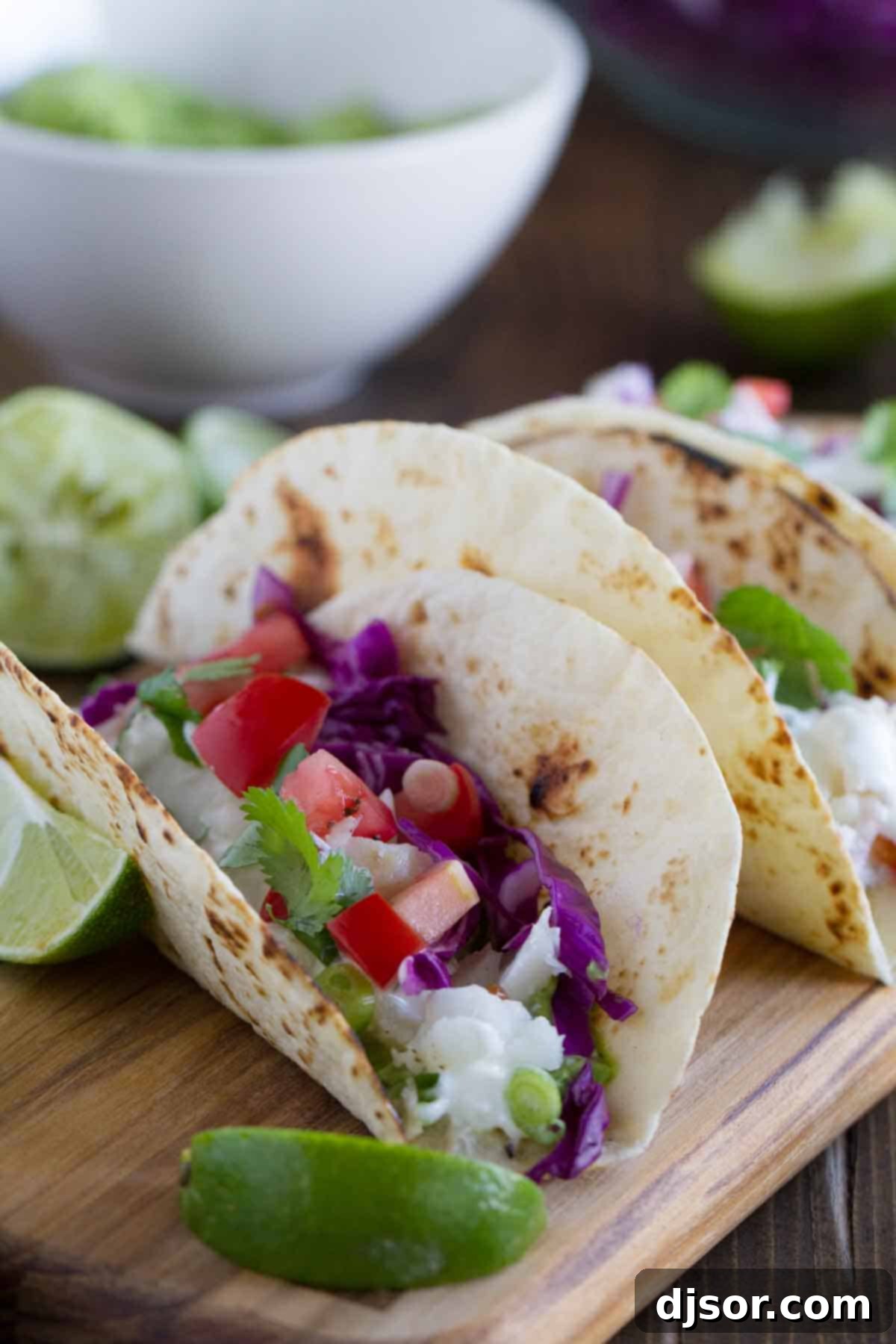 Close-up shot of a single Baja Fish Taco, perfectly assembled with grilled fish, avocado sauce, tangy mayo, and fresh toppings on a flour tortilla.