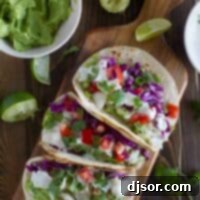 Overhead view of three beautifully arranged Baja Fish Tacos on a rustic cutting board, garnished with fresh cilantro and lime wedges.