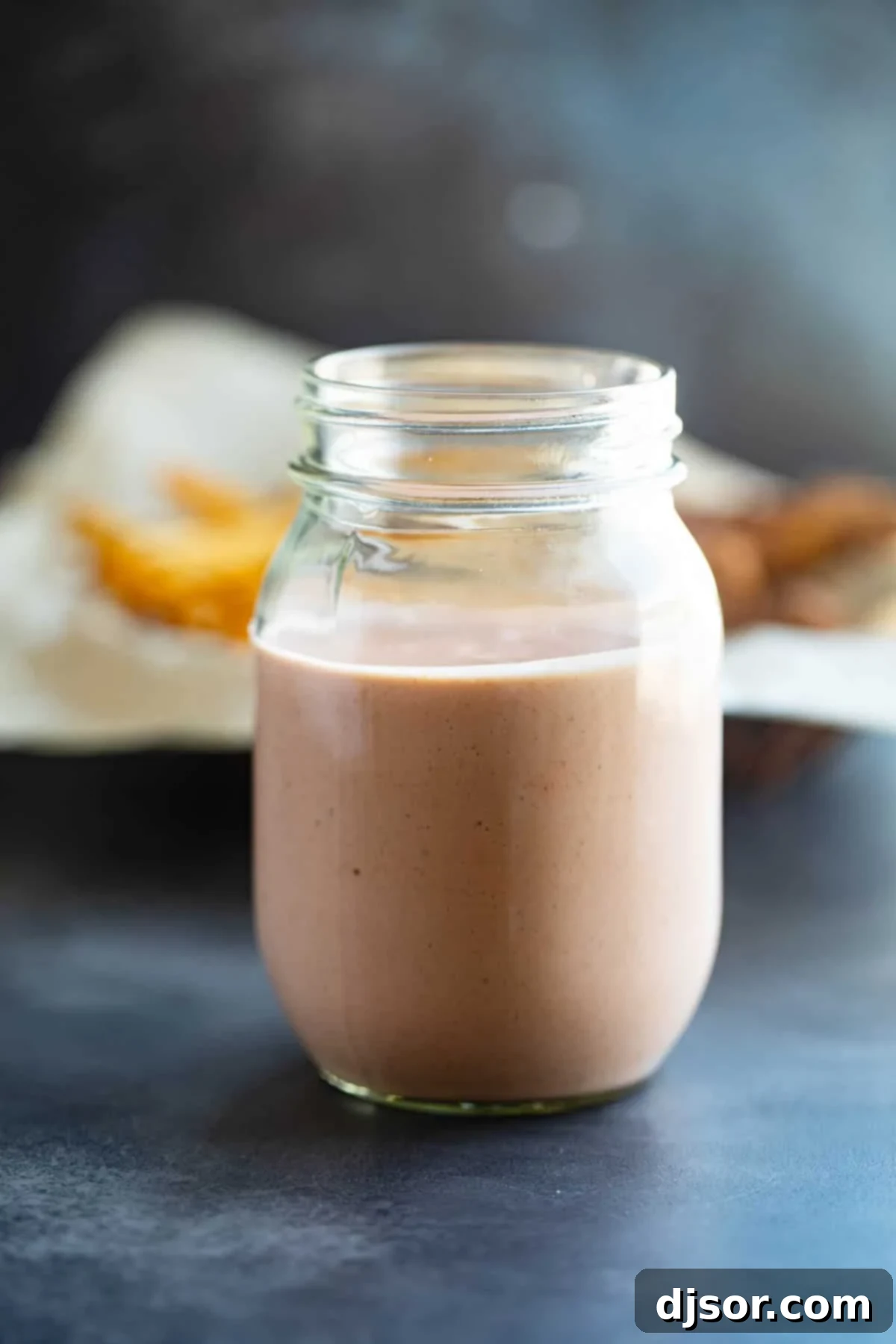 A glass mason jar filled with freshly made, creamy Comeback Sauce, set against a rustic background. The vibrant orange color of the sauce is clearly visible.