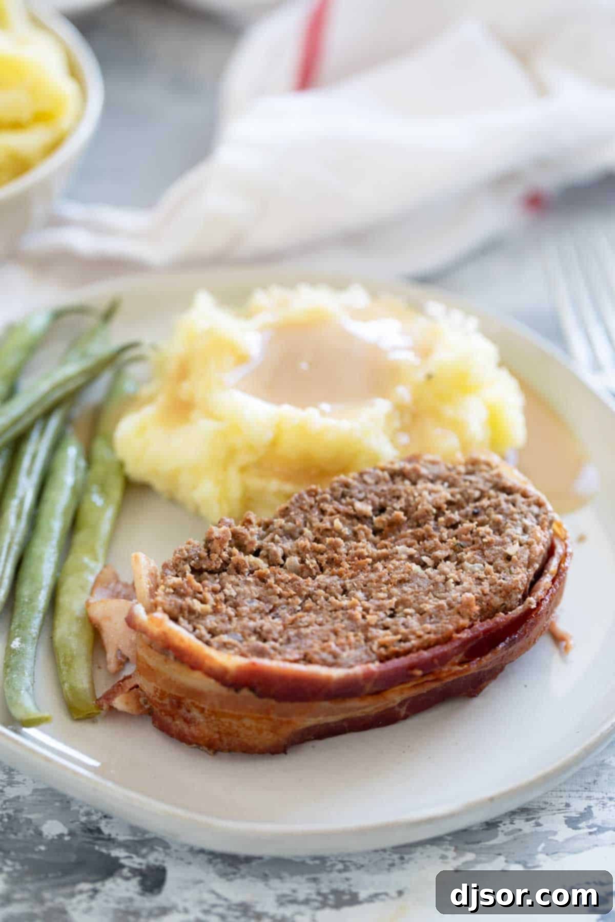 The Ultimate Bacon Meatloaf 2 Serving of Bacon Wrapped Meatloaf with sides on a plate.