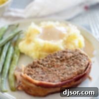 The Ultimate Bacon Meatloaf 9 Serving of Bacon Wrapped Meatloaf with sides on a plate.