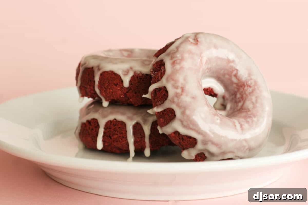 Three beautifully glazed Baked Red Velvet Donuts on a white plate, showcasing their vibrant red hue and inviting texture, ready to be enjoyed as a delightful breakfast or dessert.