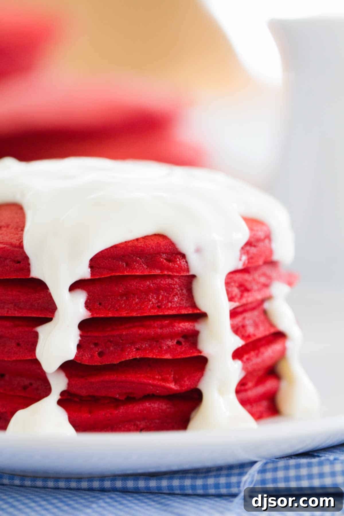 Stack of Red Velvet Pancakes with Icing A close-up view of a beautifully stacked tower of Red Velvet Pancakes, glistening with a generous drizzle of homemade cream cheese icing. The rich red color of the pancakes is prominent, highlighting their inviting texture and the decadent topping.