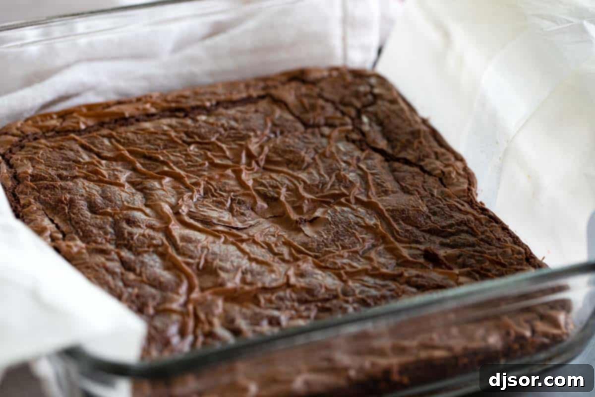 A baking dish, lined with parchment paper, filled with perfectly baked Nutella brownies, ready to be cooled and sliced.
