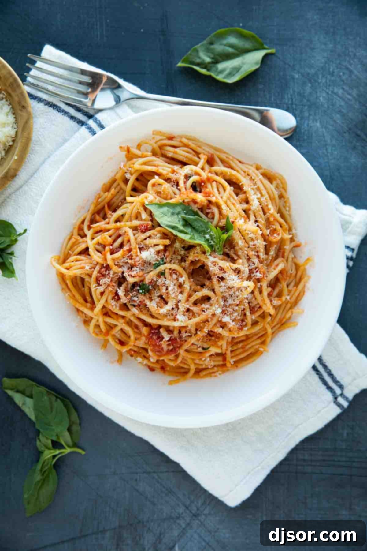 A beautifully plated bowl of garlic spaghetti, garnished with fresh basil leaves and a generous sprinkle of grated Parmesan cheese, ready to be enjoyed.