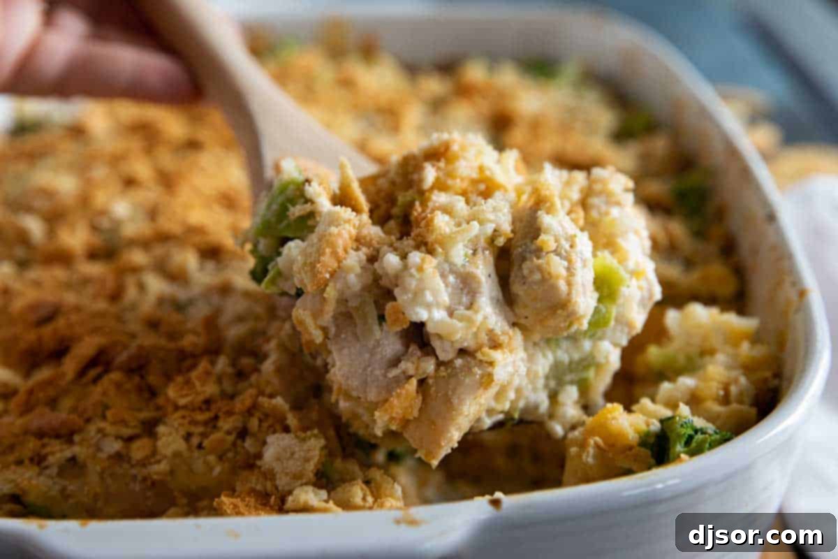A dish of creamy Chicken Divan casserole with a serving spoon, highlighting the chicken, broccoli, rice, and cheese