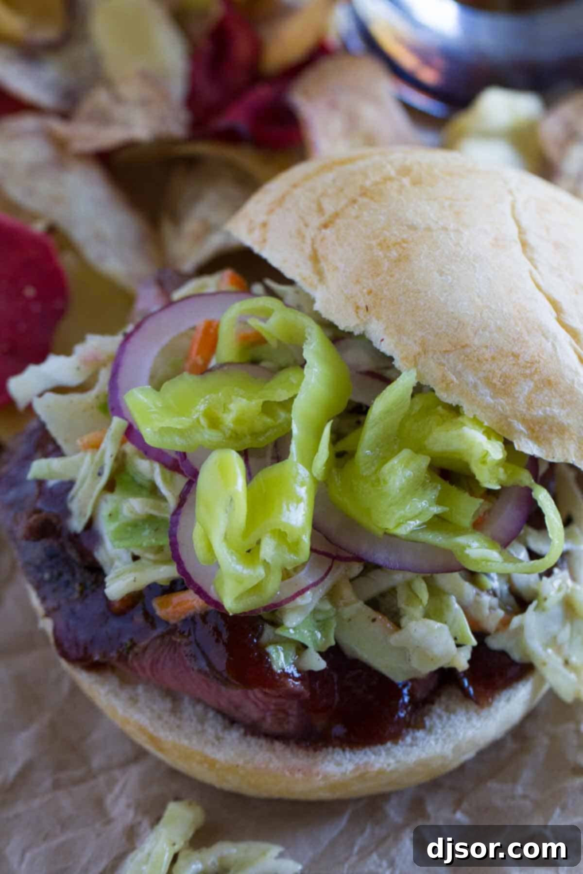 Hearty Sliced Steak Sloppy Joes with Fresh Toppings An assembled sandwich featuring sliced steak, fresh coleslaw, and a variety of colorful peppers and onions, ready to be devoured.