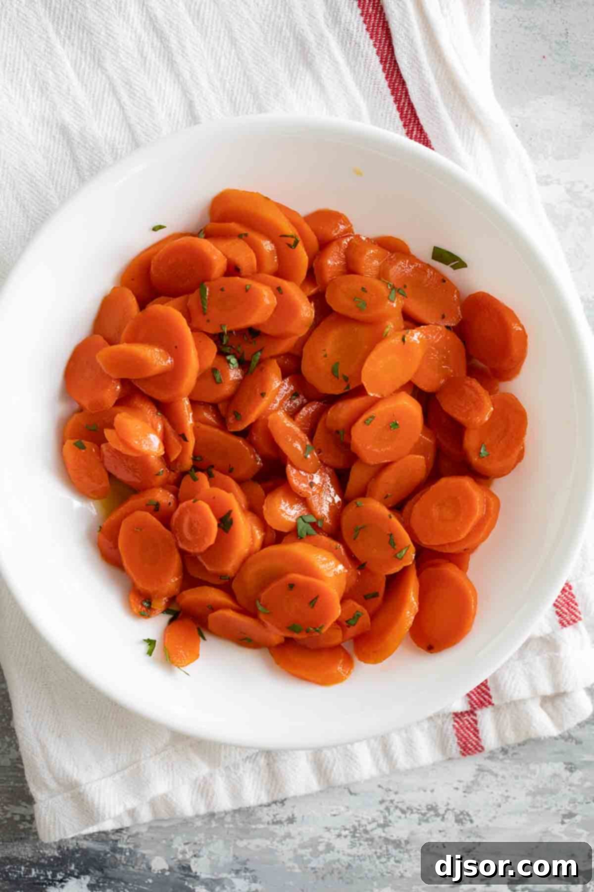 These Glazed Carrots are a simple side dish that add a bit of wow to your dinner. Cooked on the stovetop in a simple sugar and butter glaze, this carrot recipe will become a go-to! overhead view of glazed carrots in a white bowl