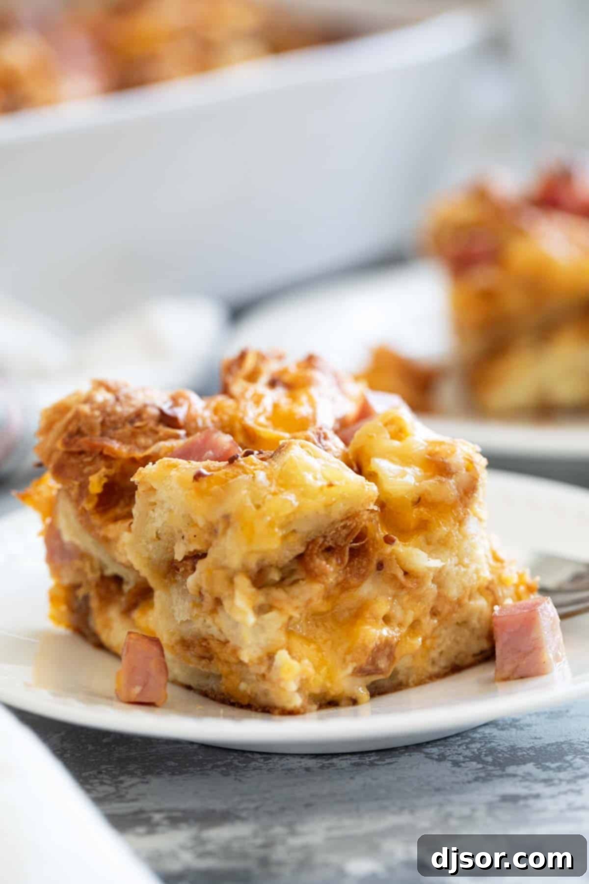 A tempting slice of Croissant Breakfast Casserole with melted ham and cheese on a plate.
